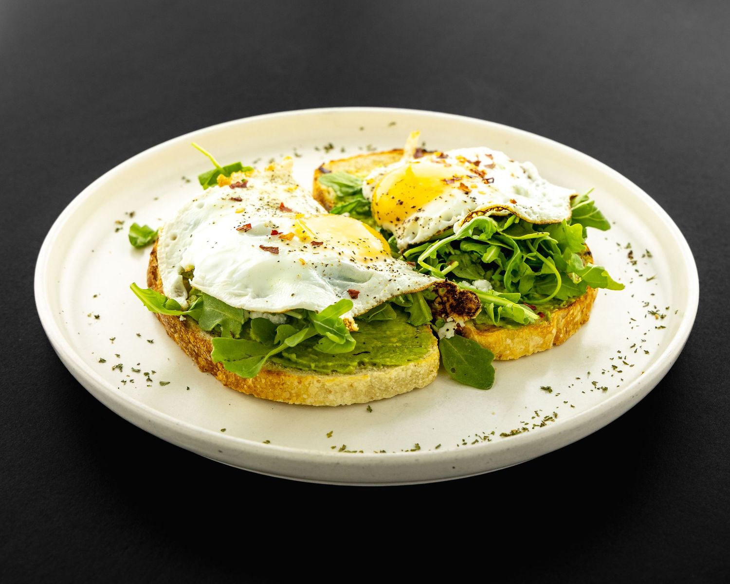 Elegant plated breakfast dishes with eggs and greens on white plates against black background.