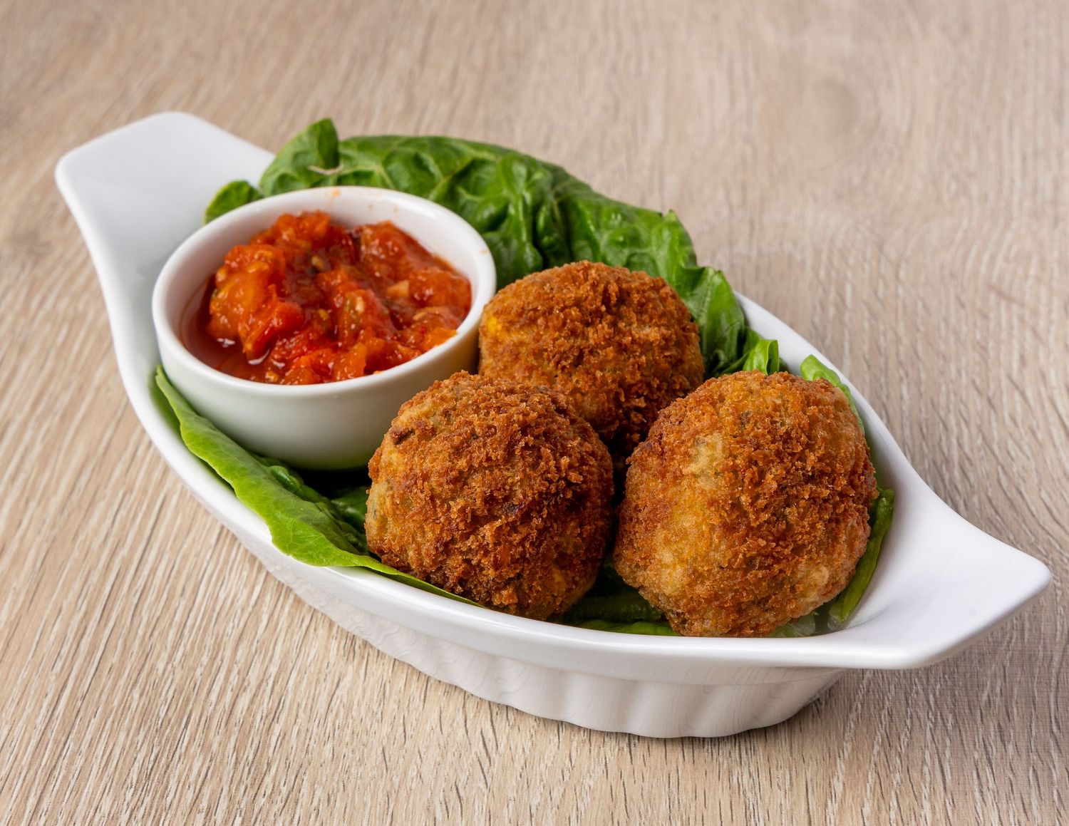 Breaded croquettes with fresh lettuce and dipping sauce on white serving plates.