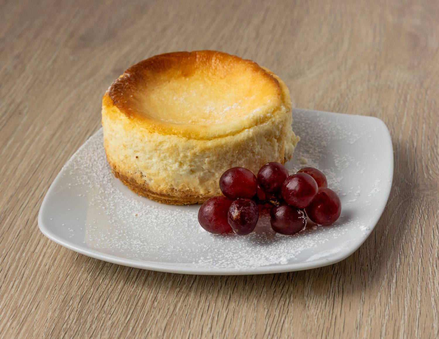 Slices of golden cheesecake garnished with red cherries on white plates.