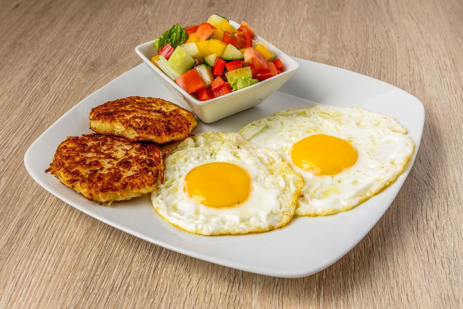 Sunny side up eggs served with colorful vegetable salad and meat patties.