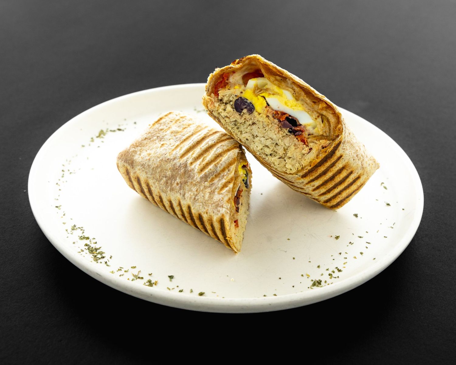 Neatly plated wraps and sandwiches garnished with herbs on white dishes.