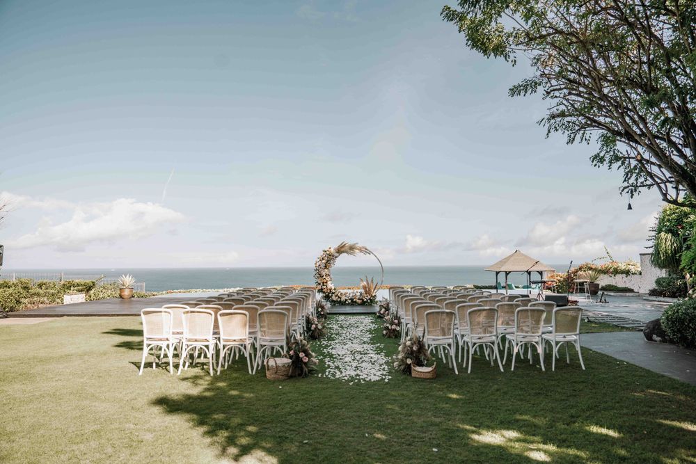 Beach wedding ceremony setup with white chairs and ocean views along the shoreline at sunset.
