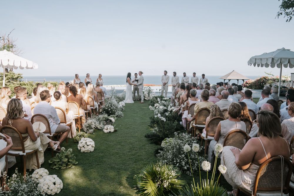Elegant outdoor wedding reception seating and dining areas with ocean views in a sun-drenched tropical garden setting.