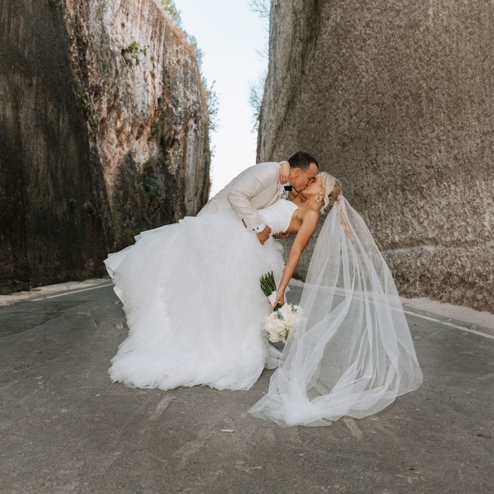 Two people in wedding attire share an intimate moment between tall concrete walls during a romantic photoshoot.