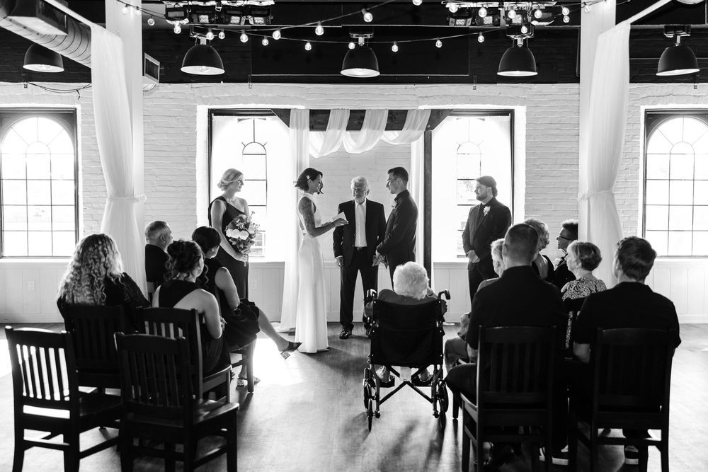 People gather at tables in a bright modern event venue with industrial-style ceiling and large windows.