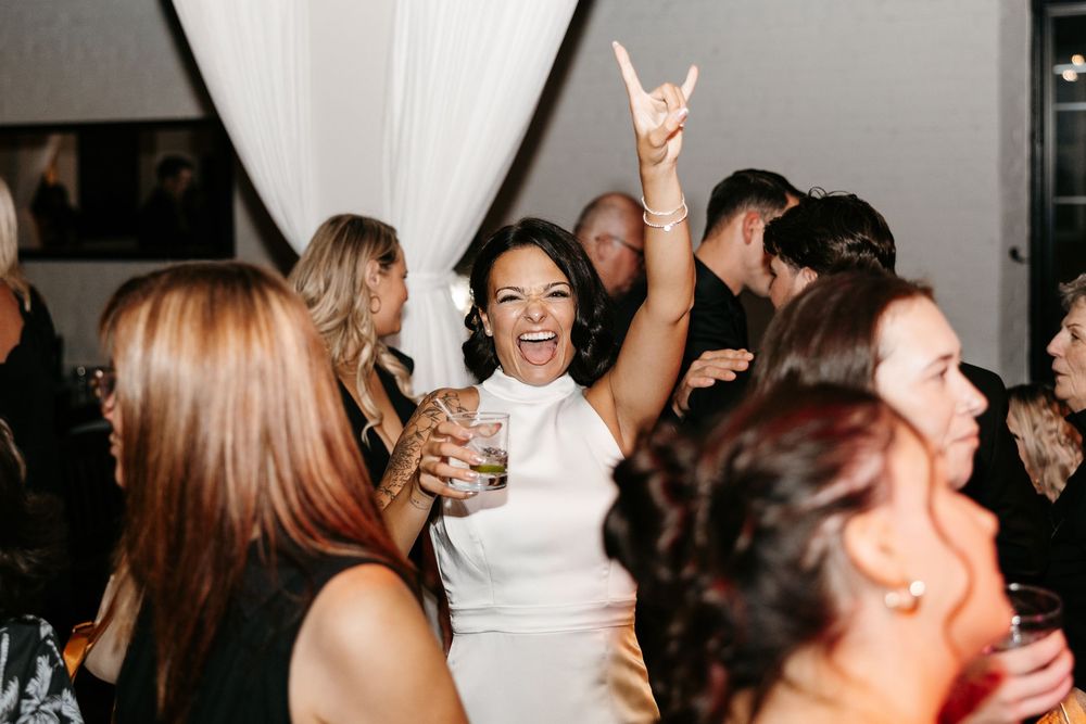 A black and white photograph shows people dancing and laughing together at what appears to be a party or celebration.