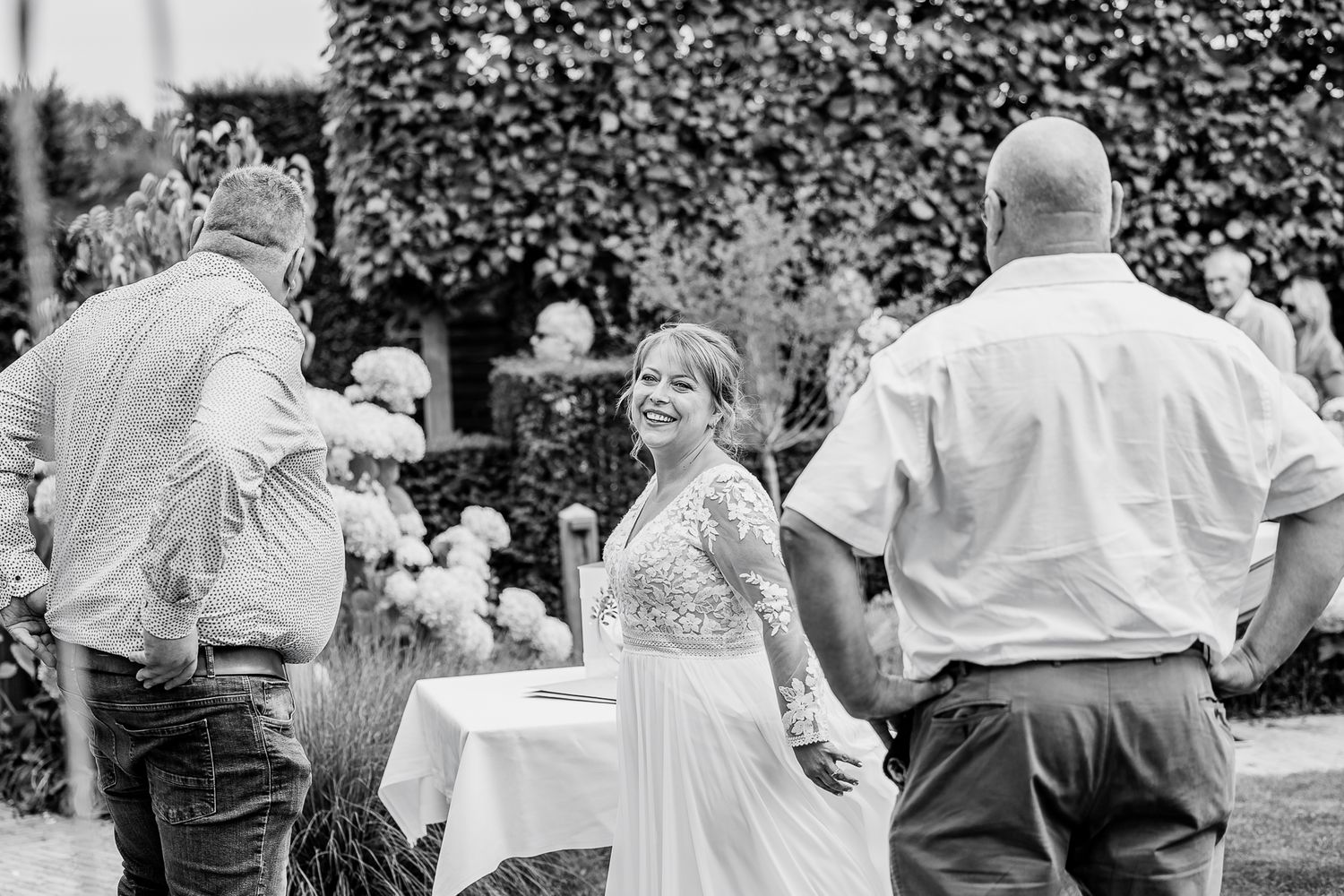 Black and white wedding photo capturing joyful guests mingling at an outdoor garden reception.