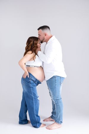 A couple wearing matching white tops and blue jeans pose together in artistic dance-like positions against a white backdrop.