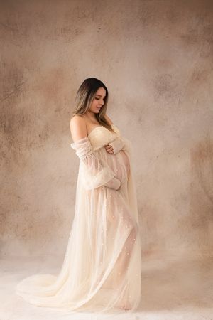 A series of dreamy maternity photos showing a woman in a flowing white dress against a textured beige backdrop.