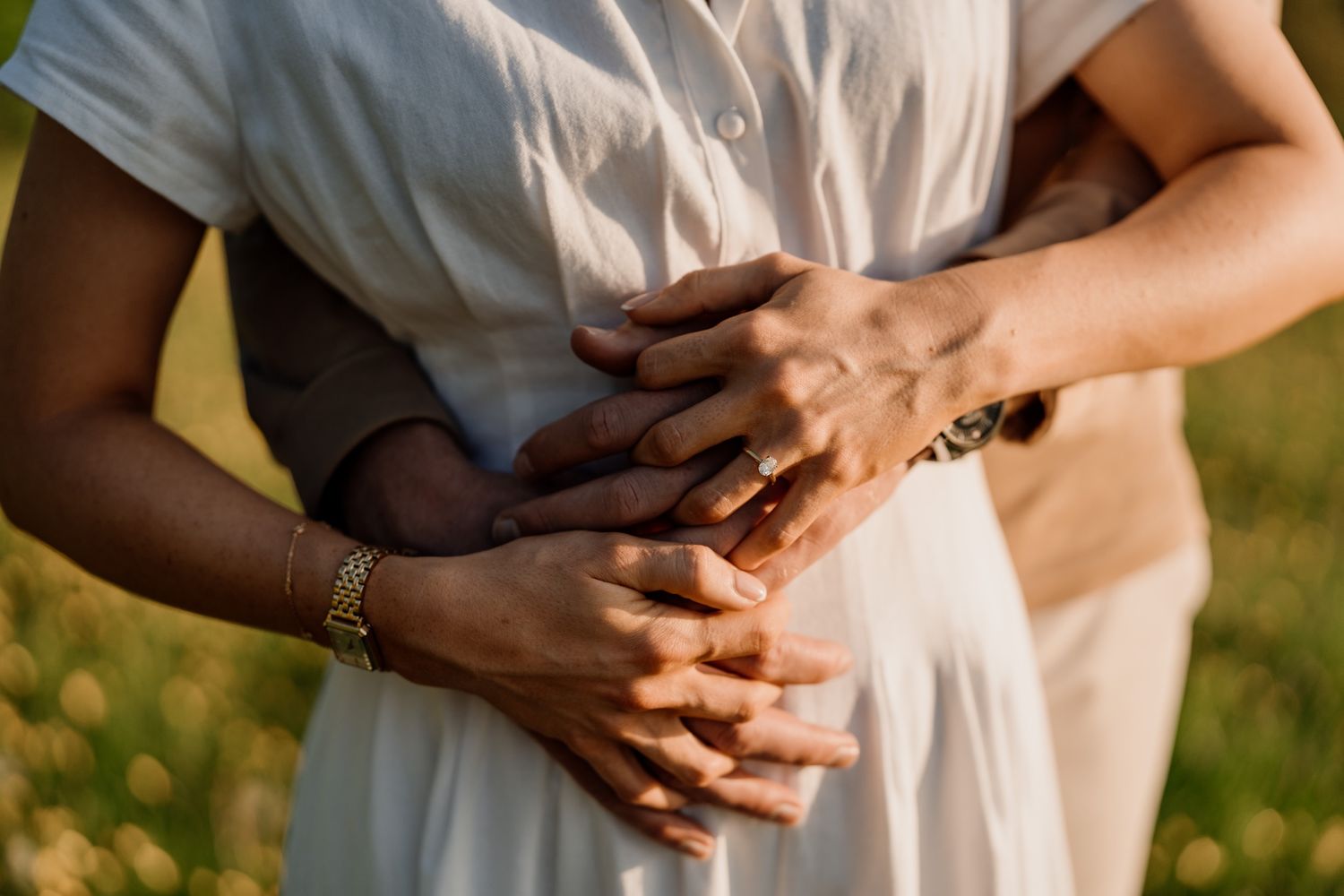 Close-up of hands tenderly embracing in a sunny outdoor meadow with golden natural lighting.