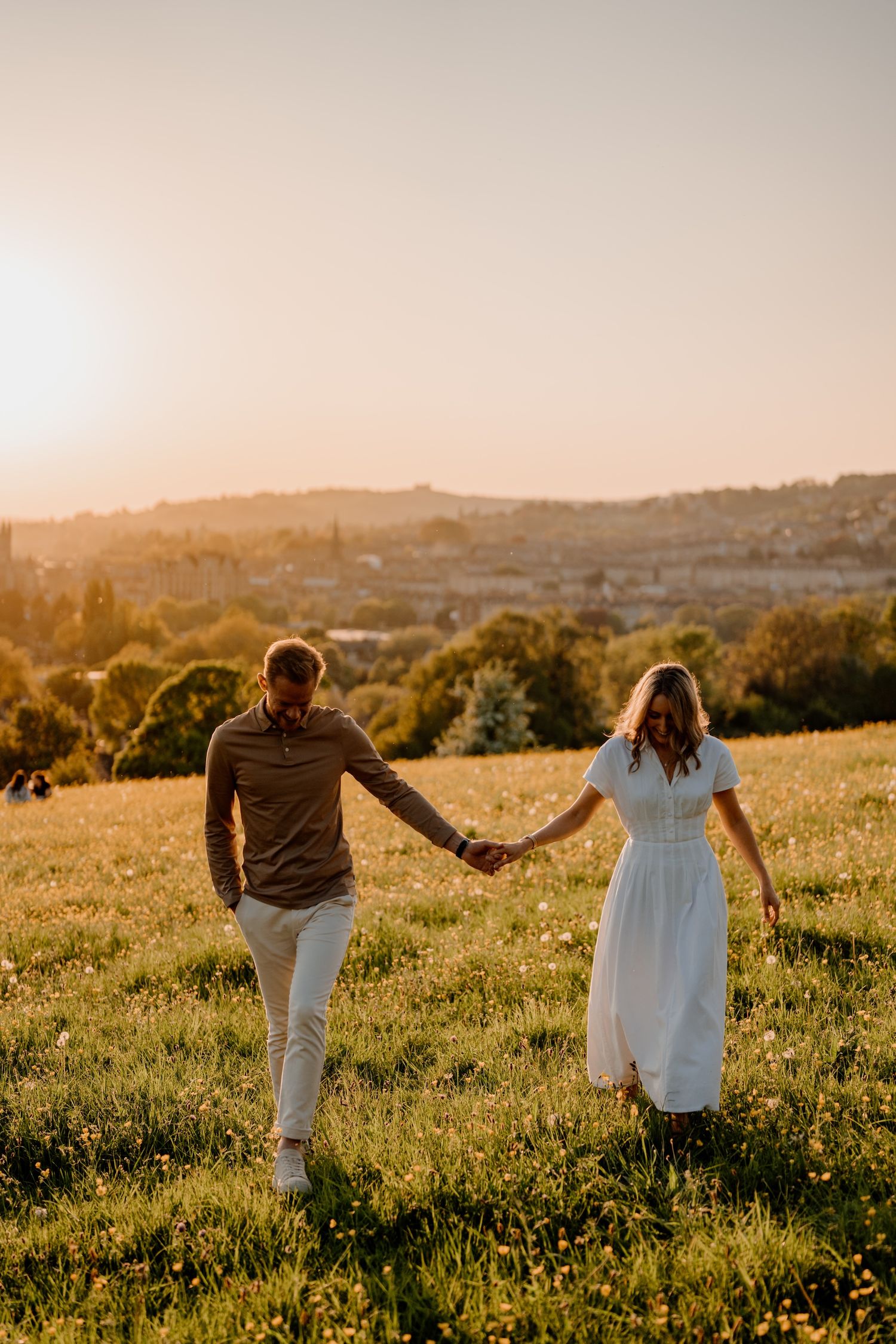 Couple holding hands while walking through a golden meadow at sunset in the hills.