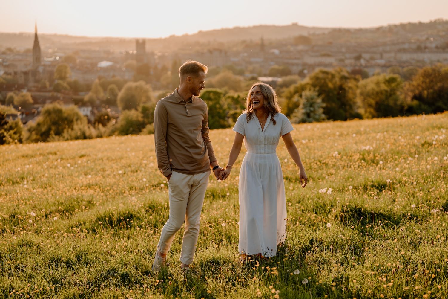 Silhouetted couple holding hands while walking through a sunlit golden meadow at sunset.
