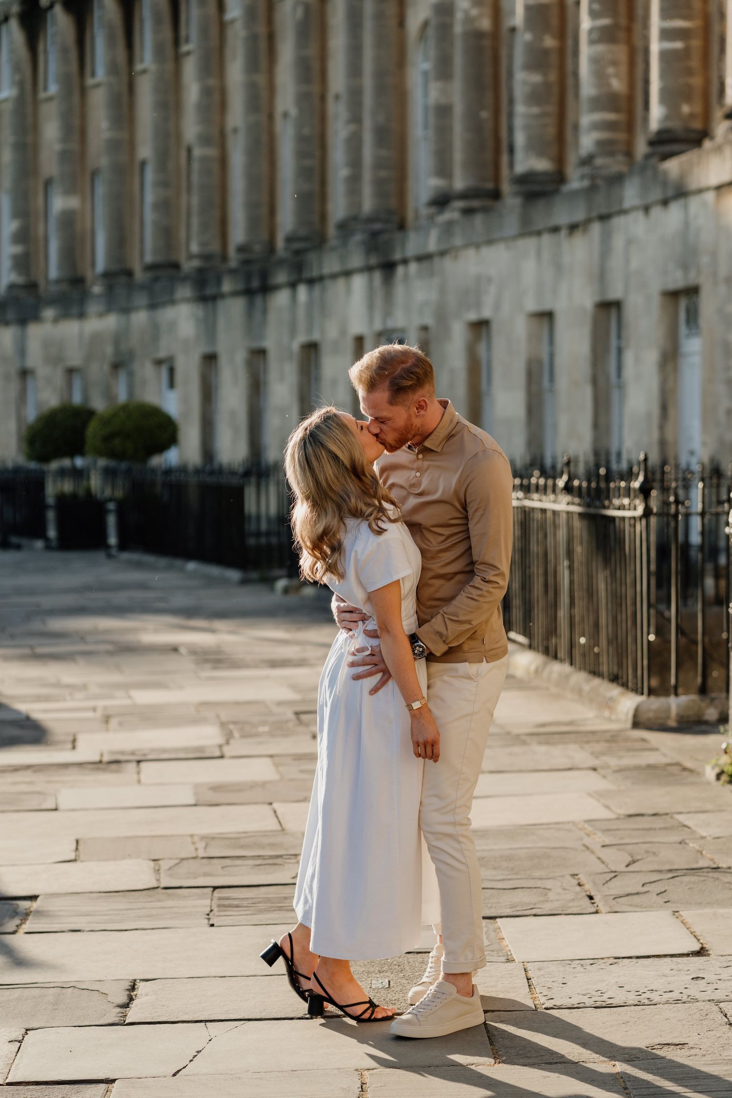 A couple in casual attire shares romantic moments on a historic city street with elegant stone architecture.