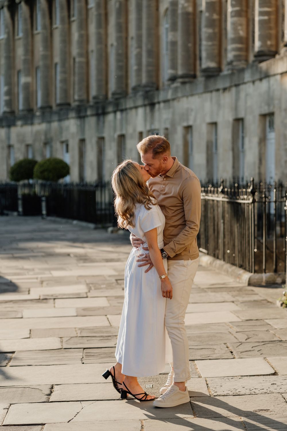 A couple in casual attire shares romantic moments on a historic city street with elegant stone architecture.