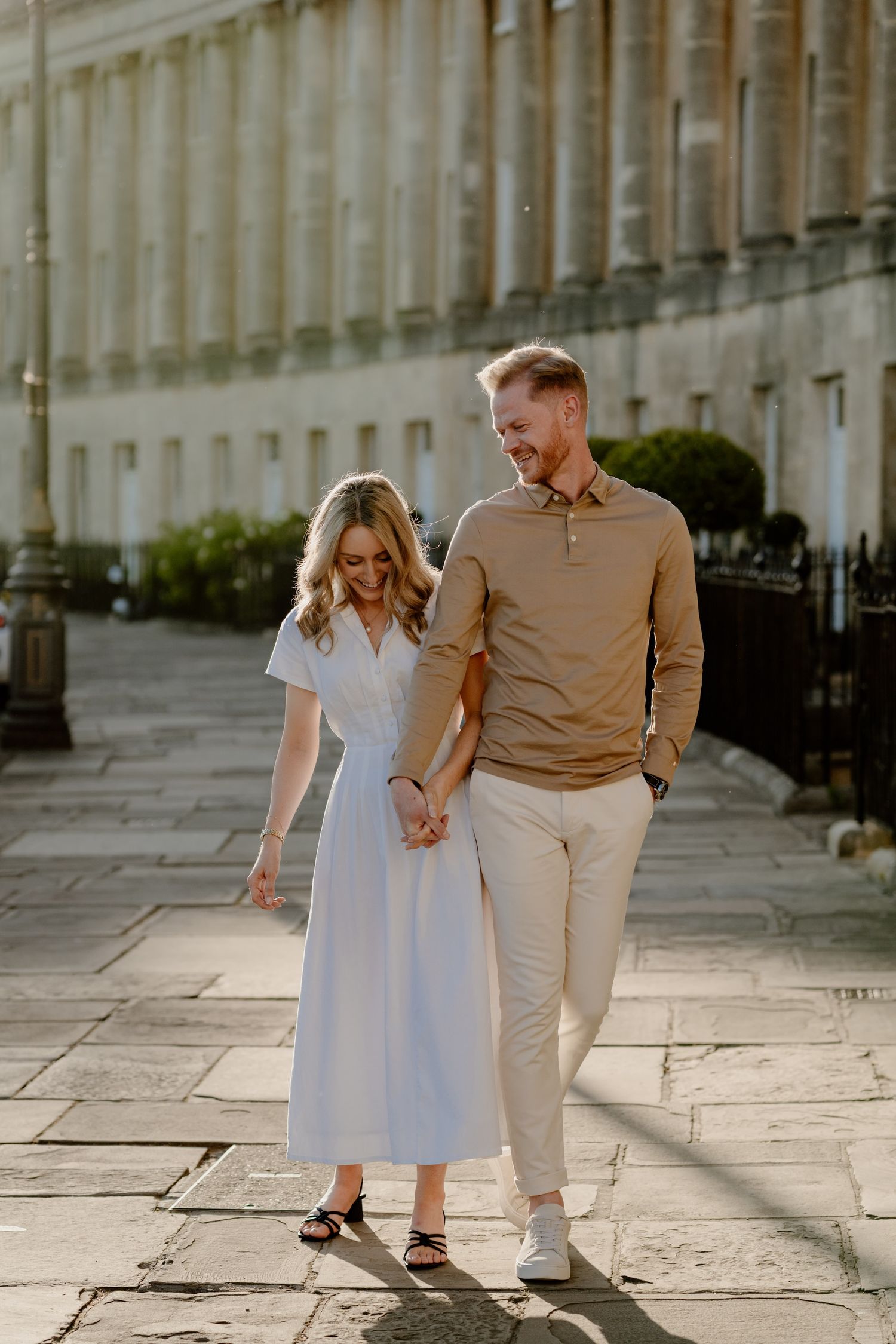 A couple shares a romantic moment on a stone walkway in front of an elegant Georgian-style building.