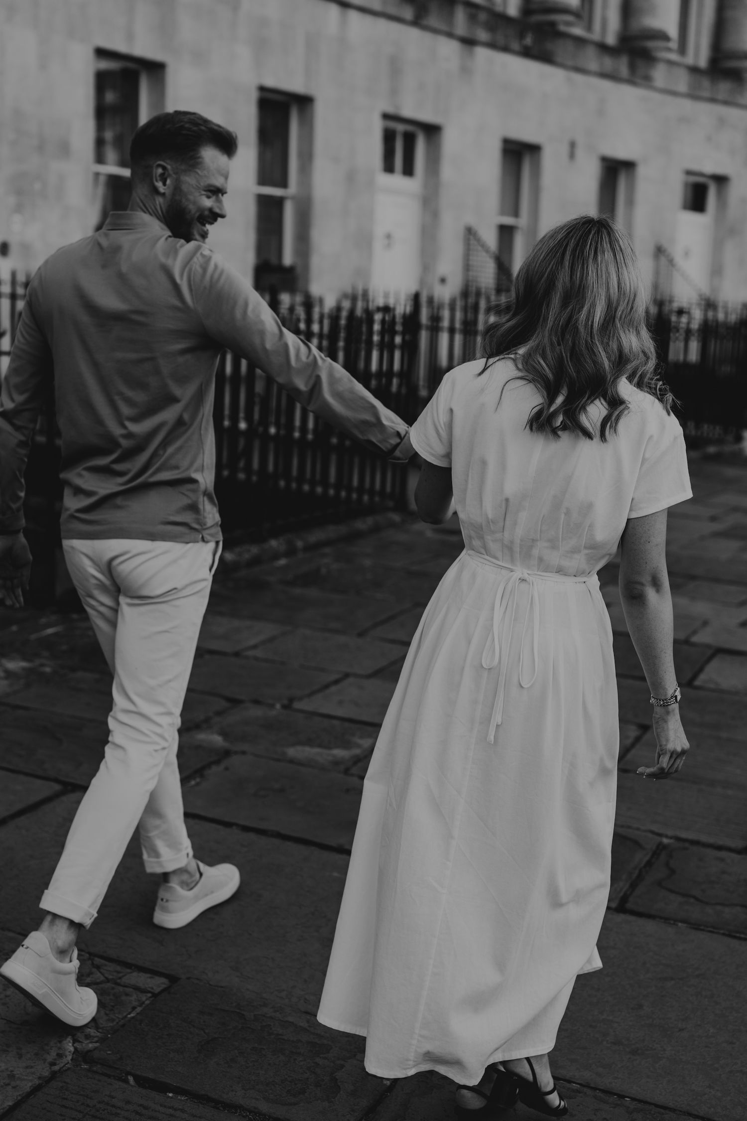 A couple in casual attire walking together on a stone walkway, captured in black and white.