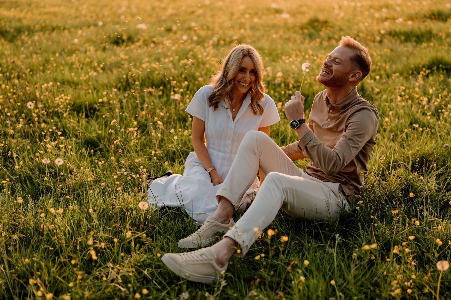 Couple sits together in a golden meadow at sunset while sharing intimate moments and conversations.