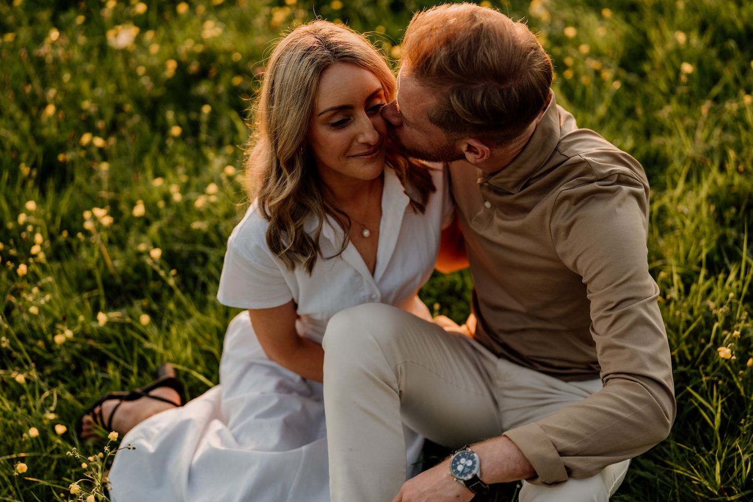 A couple sits intimately in a meadow of yellow wildflowers during golden hour.