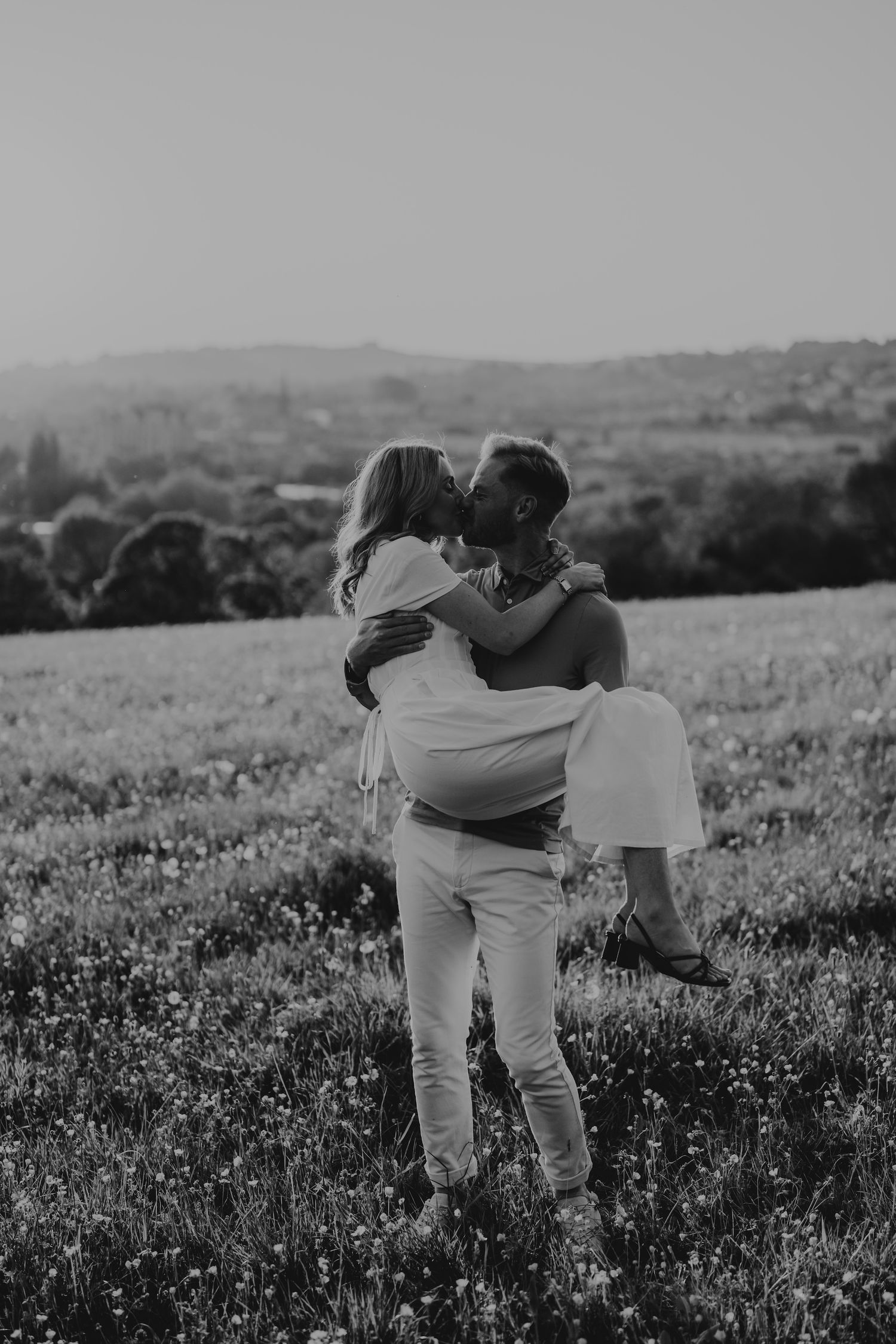 Monochrome sequence of a couple embracing in a wildflower meadow with rolling hills in the background.