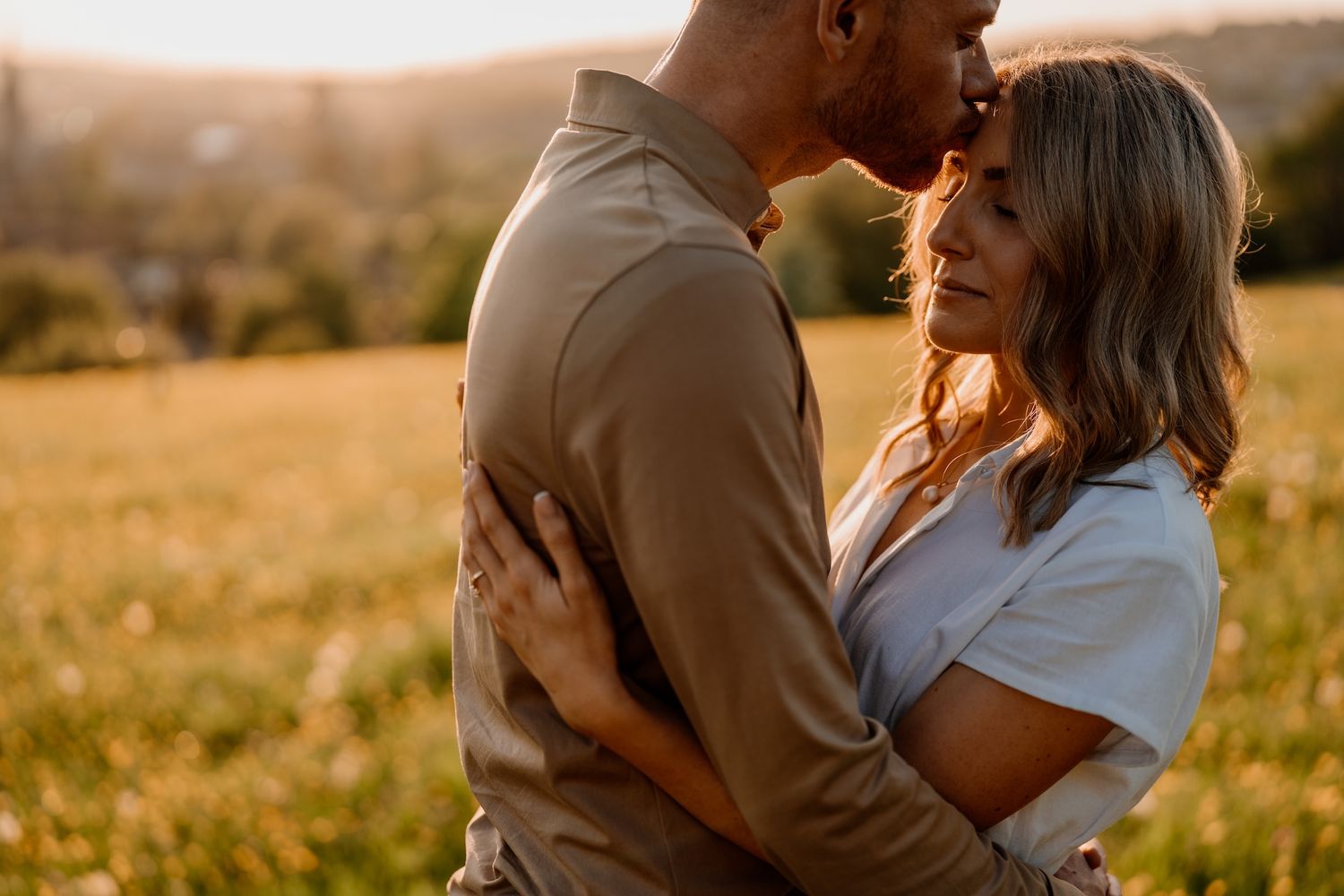 A happy couple embraces in a golden sunlit field during sunset, creating a romantic silhouette.