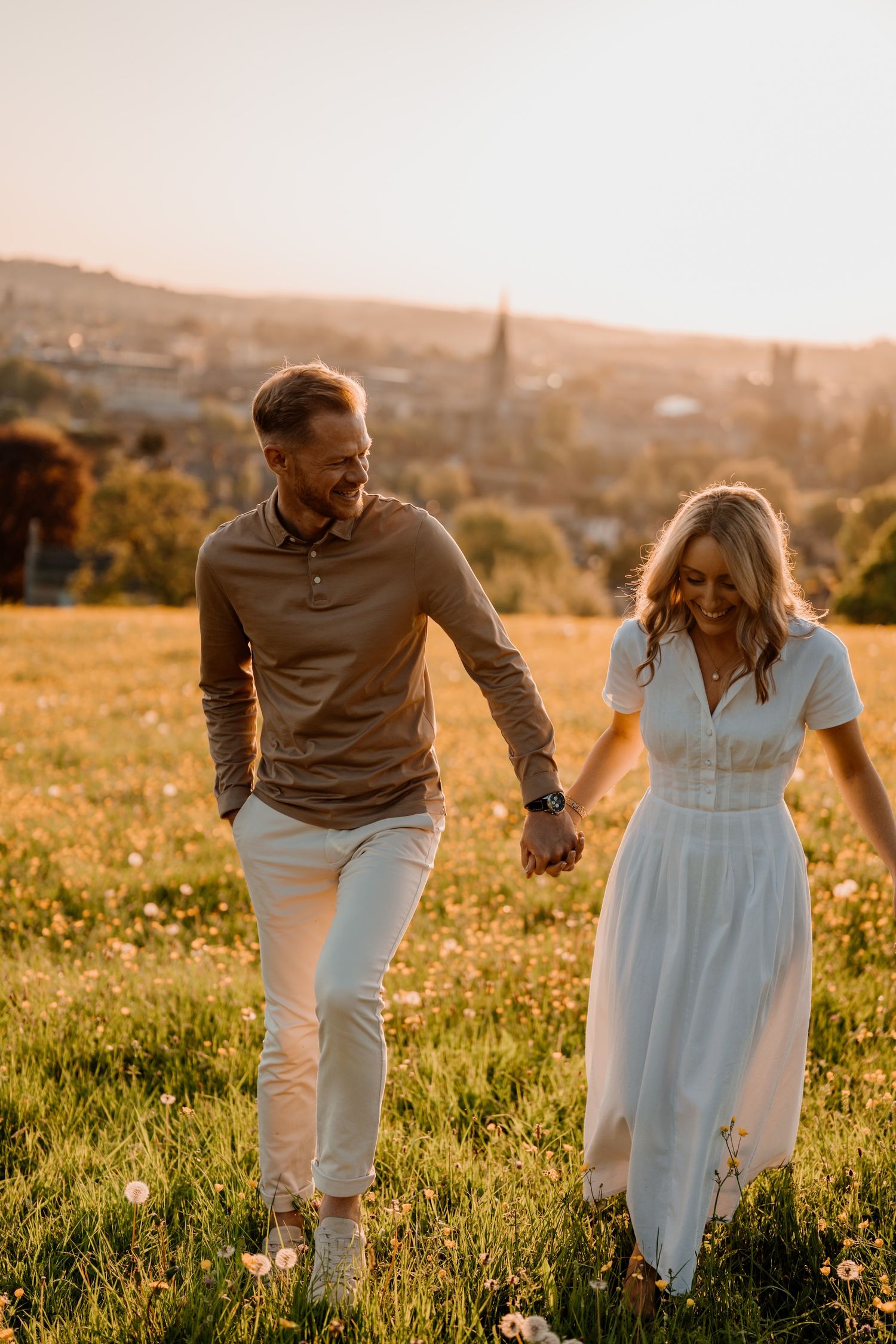 Two people wearing coordinated light-colored outfits dance together in a field at sunset.