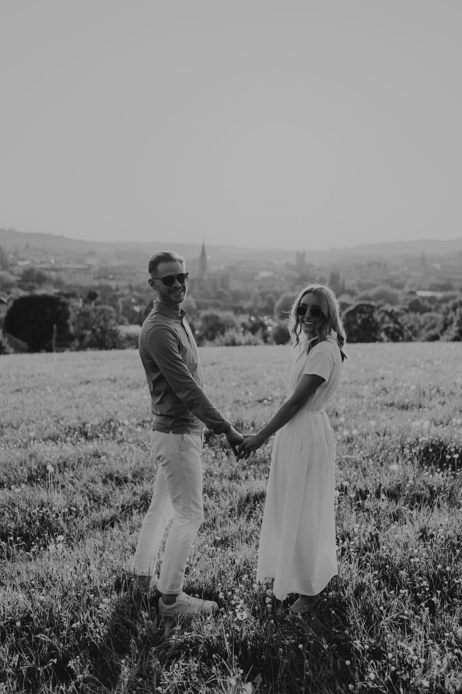 Black and white photo of a couple dancing together in a blooming meadow against a rolling landscape.