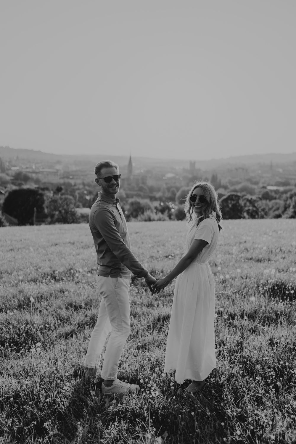 Black and white photo of a couple dancing together in a blooming meadow against a rolling landscape.