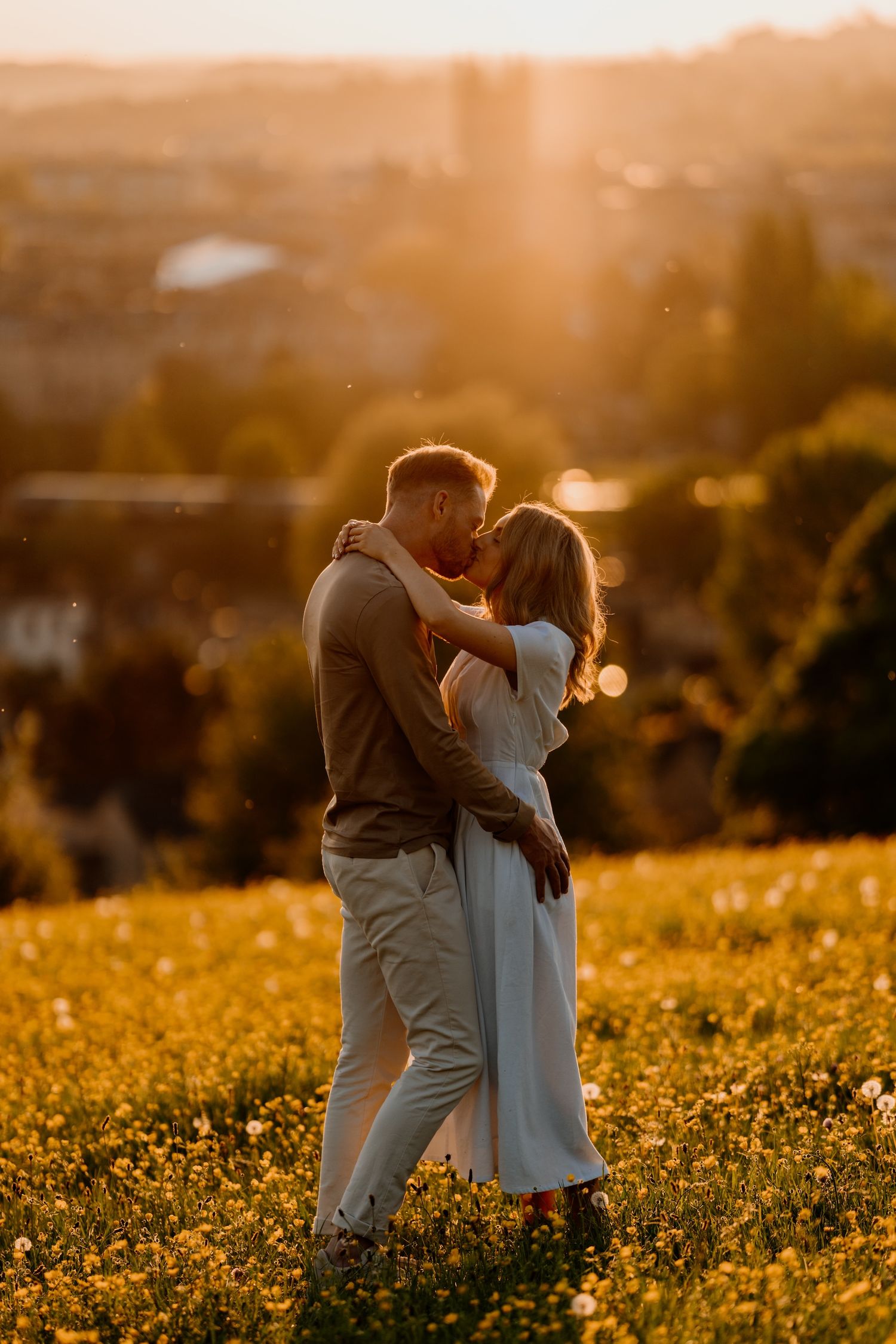 A romantic couple embraces in a golden wildflower field at sunset creating a dreamy silhouette against the warm light.
