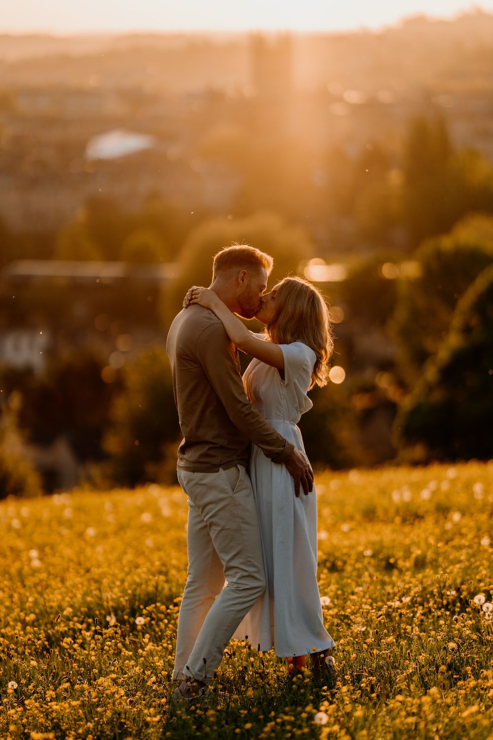 A romantic couple embraces in a golden wildflower field at sunset creating a dreamy silhouette against the warm light.