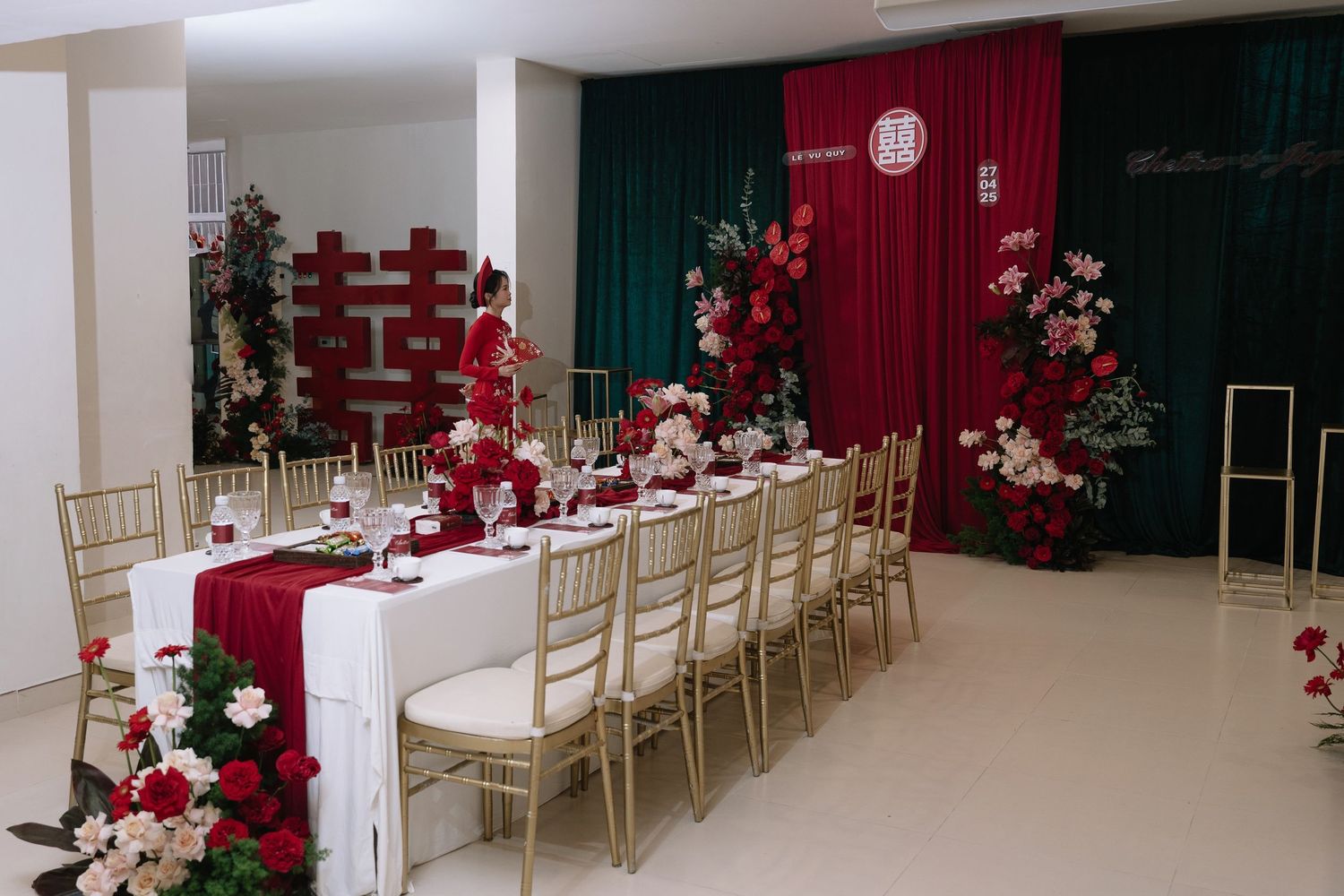 Red and white Vietnamese wedding reception with long table, gold chairs, and floral decor.