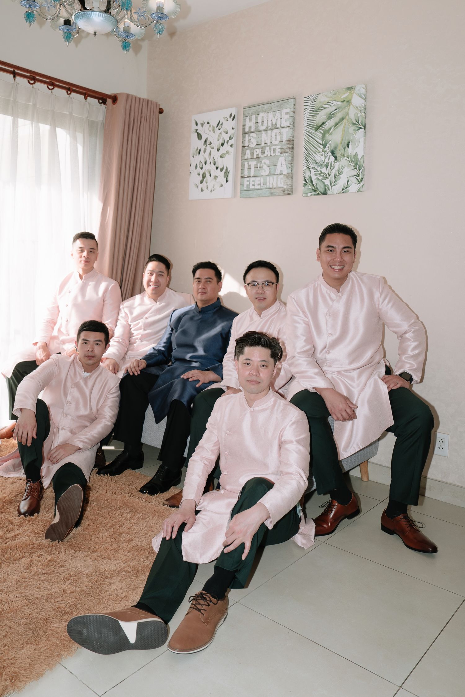 Groom in navy ao dai posing with groomsmen in pink traditional Vietnamese attire in a bright room.