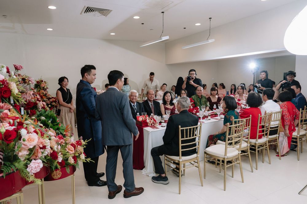 Guests mingling at an elegant Vietnamese wedding reception with red and pink floral arrangements.