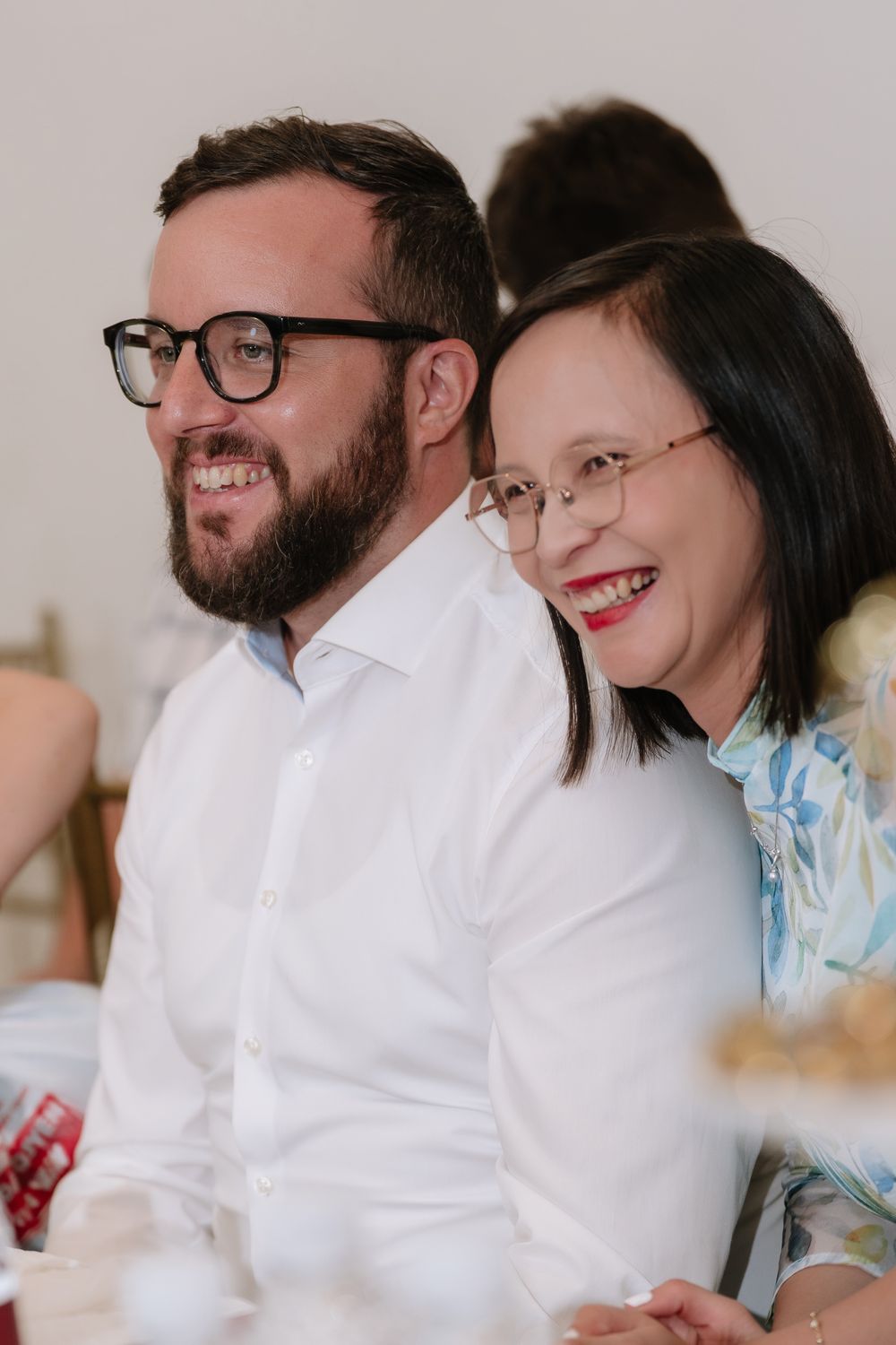 Smiling couple wearing glasses enjoying a wedding reception in a bright venue.