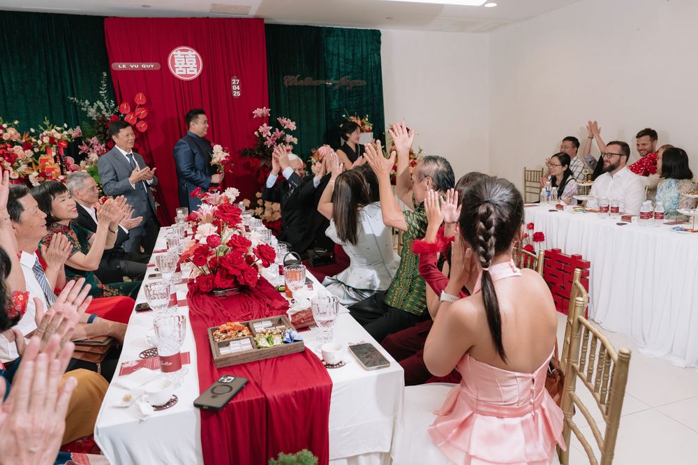 Wedding guests raising hands and applauding at a festive Vietnamese wedding ceremony with red decor.