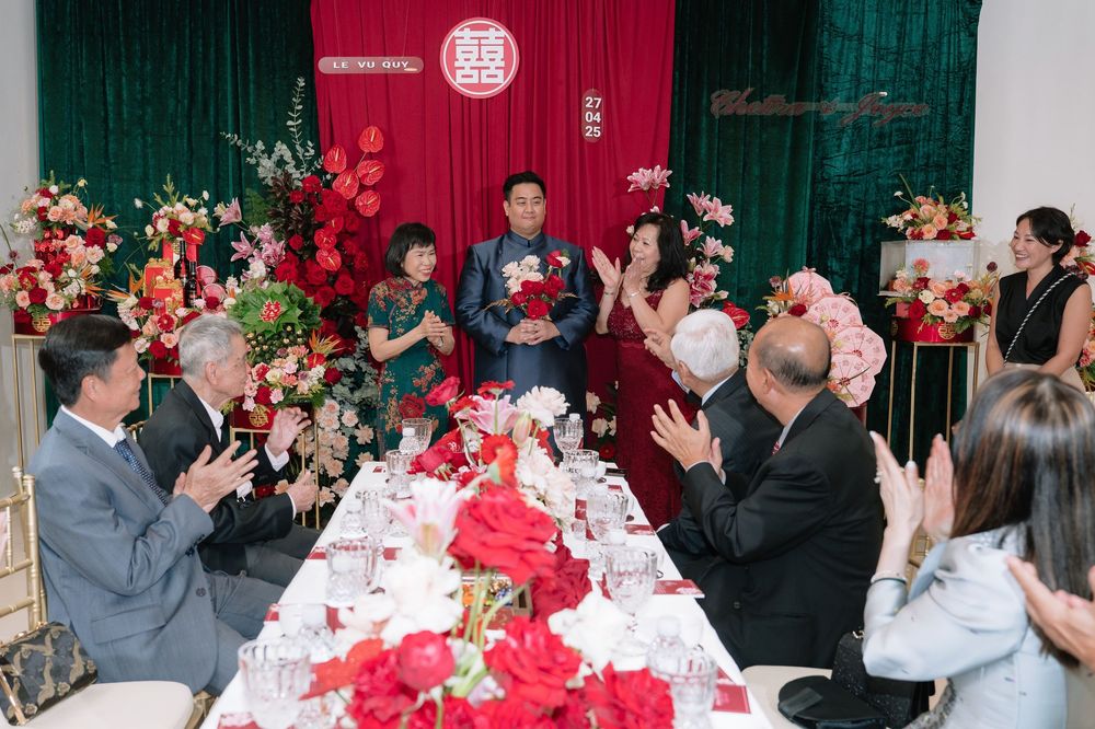 Guests applaud a couple during a traditional Chinese wedding banquet with red floral decor.