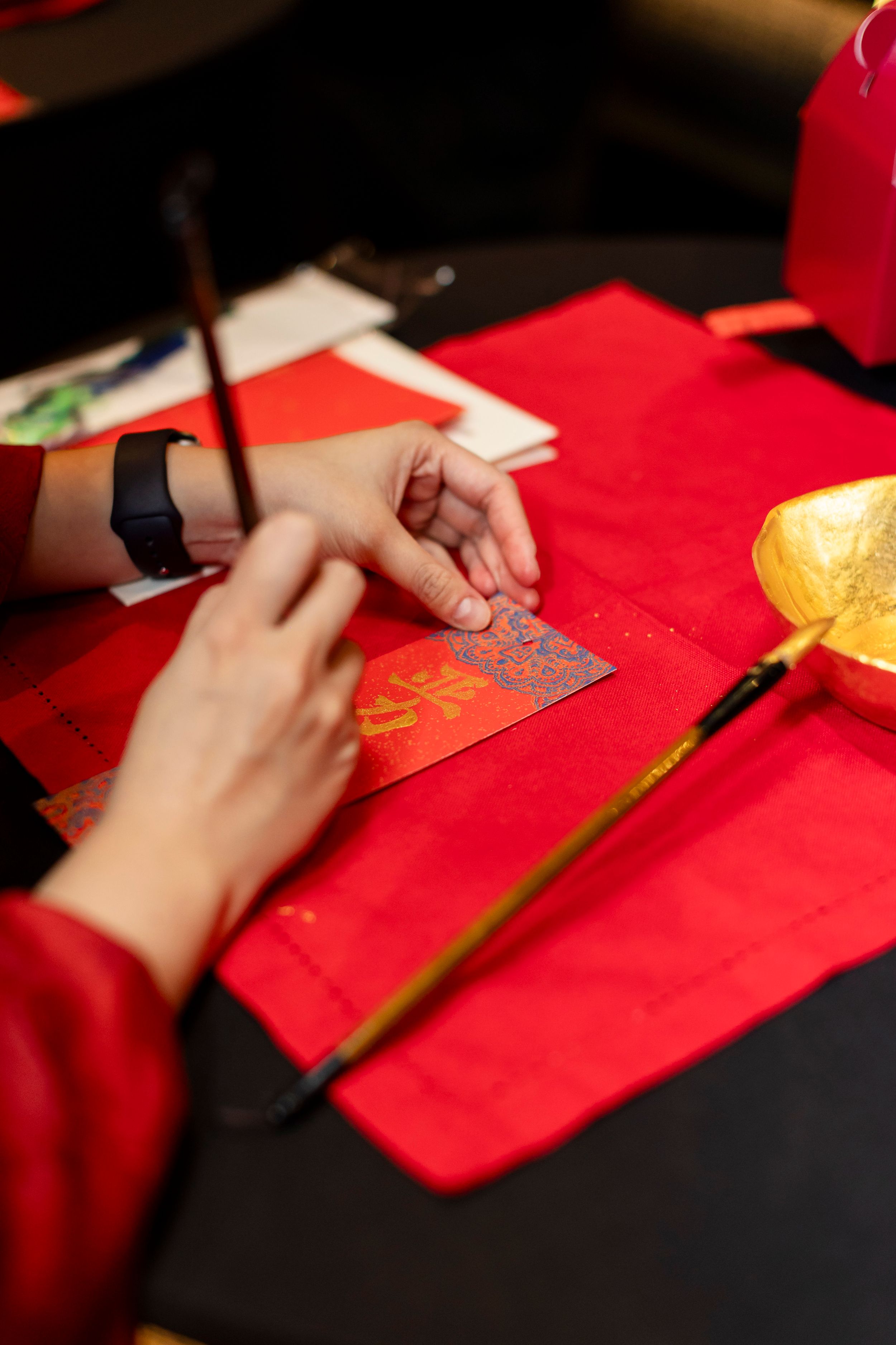 Hands writing on red envelope with gold ink for Chinese New Year tradition.