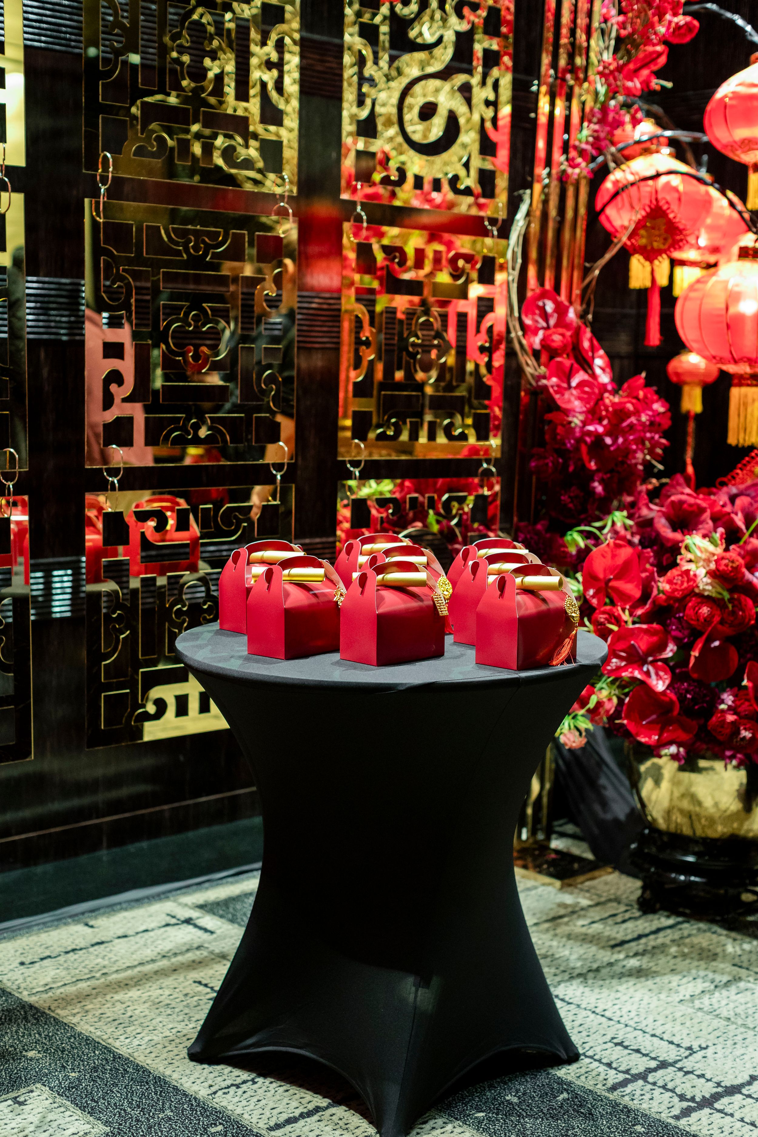 Red gift boxes displayed on black cocktail table with oriental screen and lanterns in background.