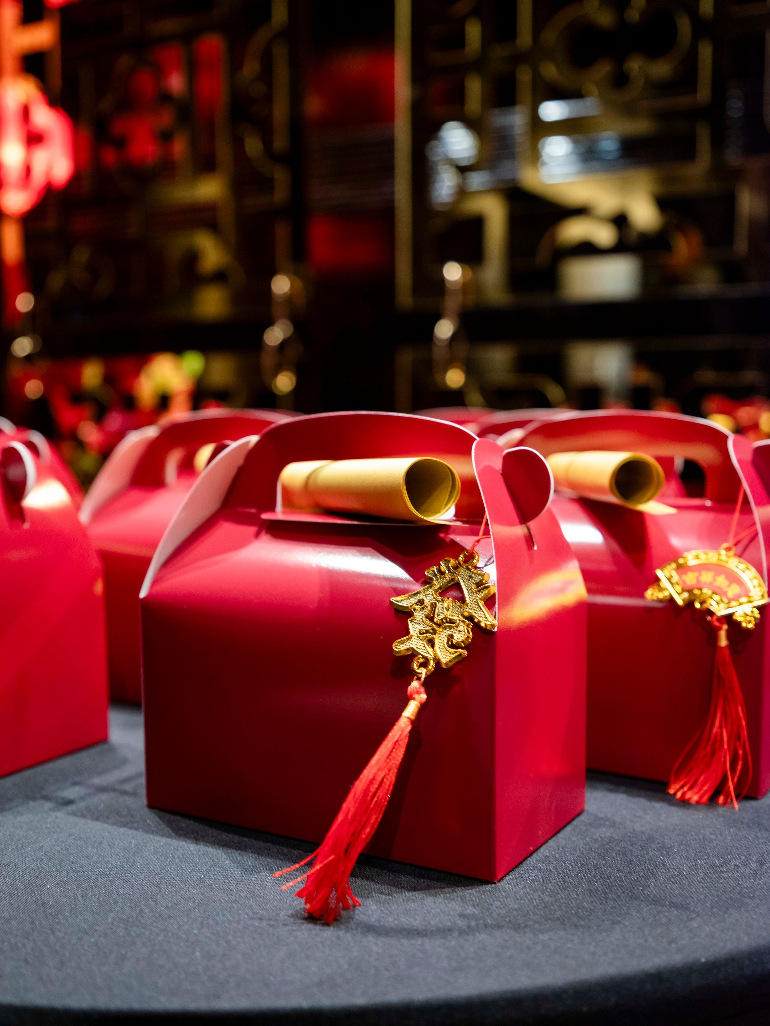 Row of red gift boxes with gold scrolls and tassels on dark table.
