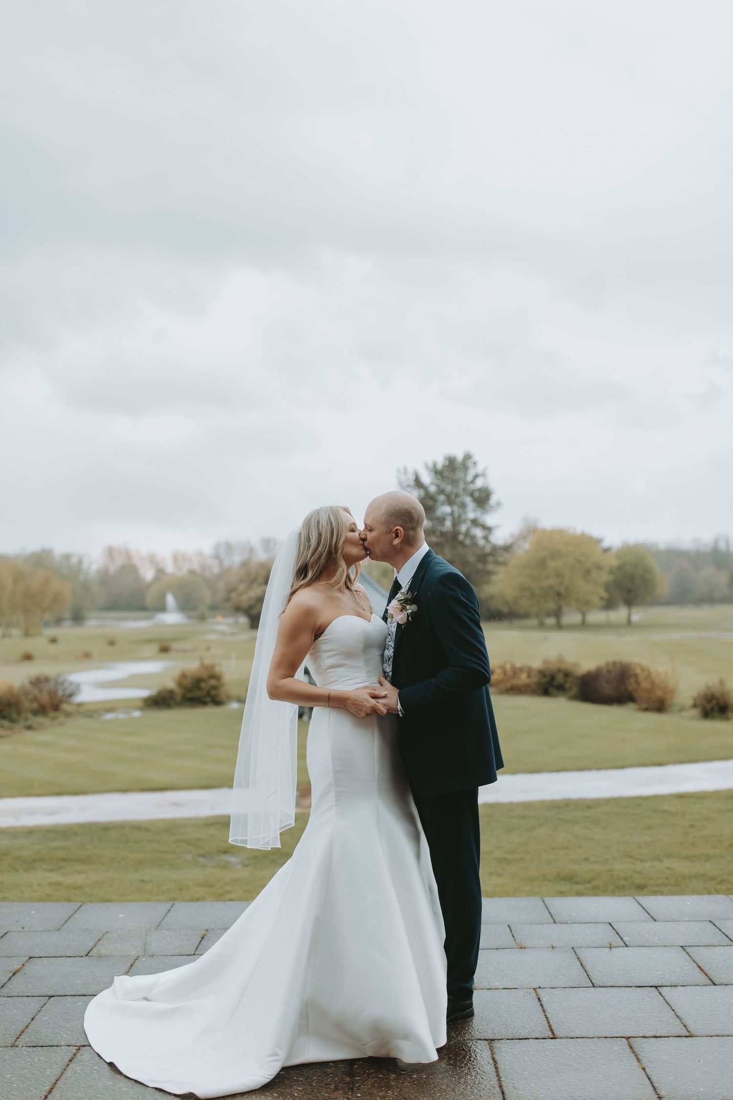 A romantic wedding couple shares an intimate moment on a stone patio overlooking a scenic countryside landscape.
