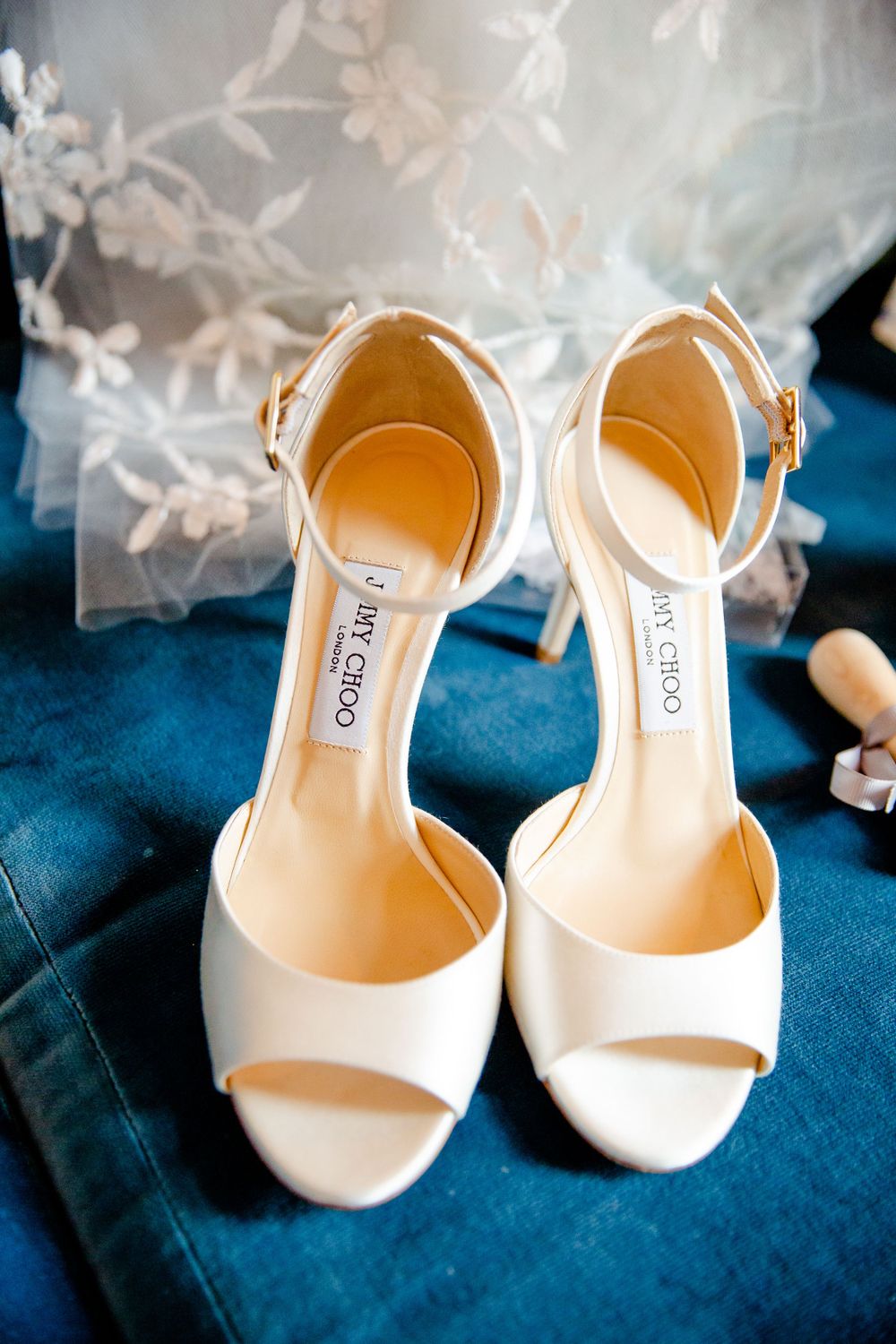 Classic white Jimmy Choo bridal shoes displayed on blue velvet fabric.