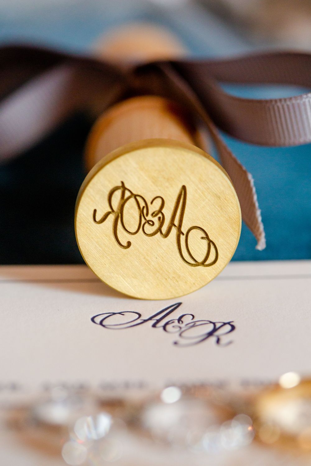 Elegant monogram wax seal with brown ribbon on wedding stationery.