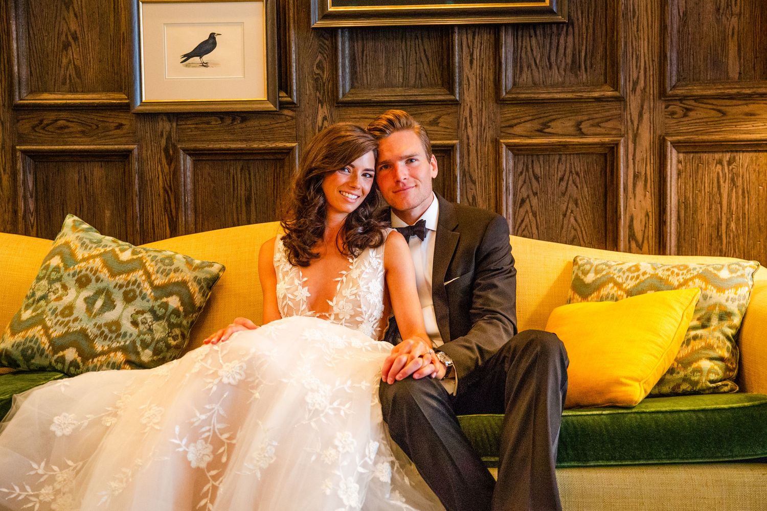 An intimate wedding portrait on a yellow velvet couch with wood-paneled walls.