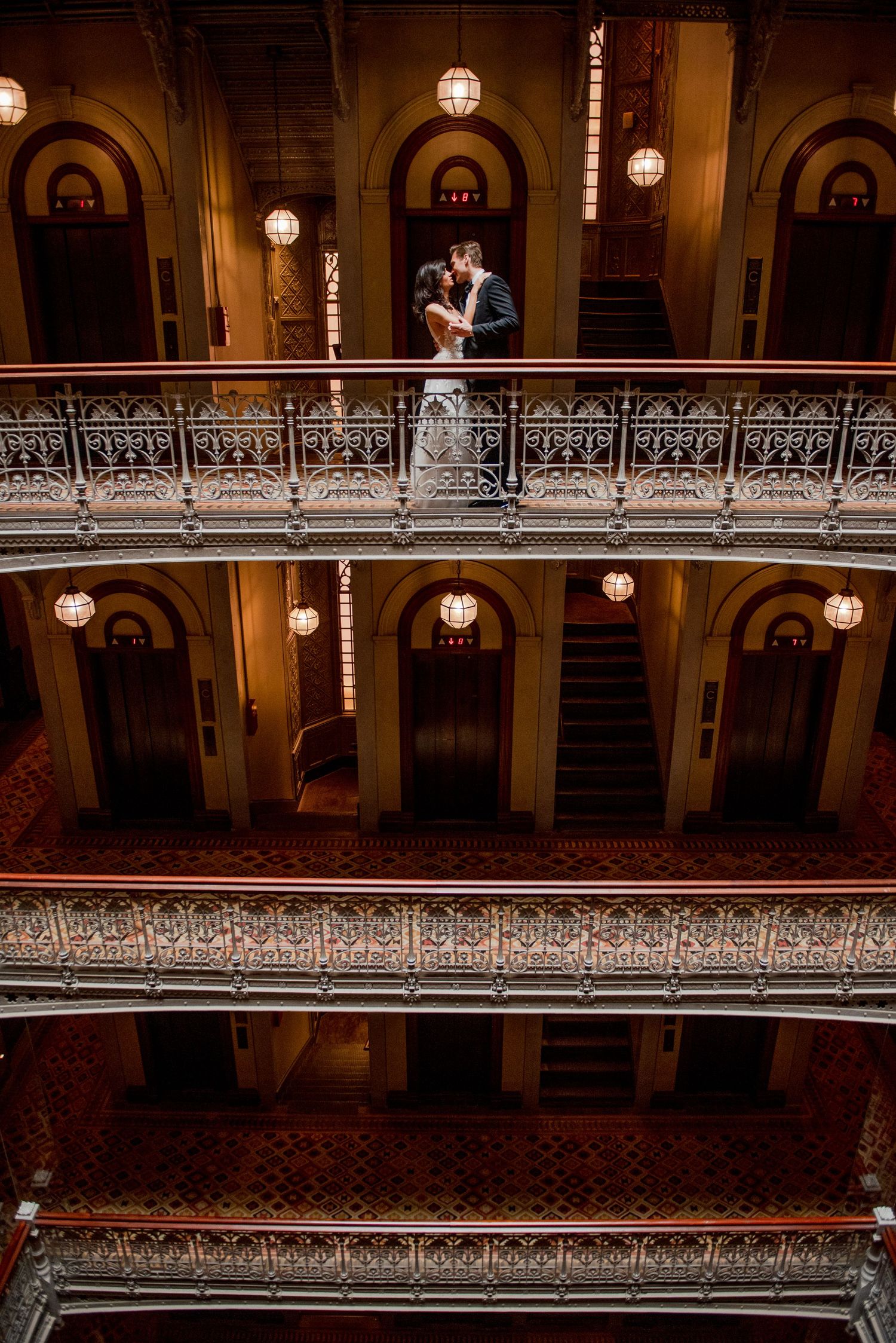 A romantic wedding moment captured on a vintage balcony with glowing pendant lights.