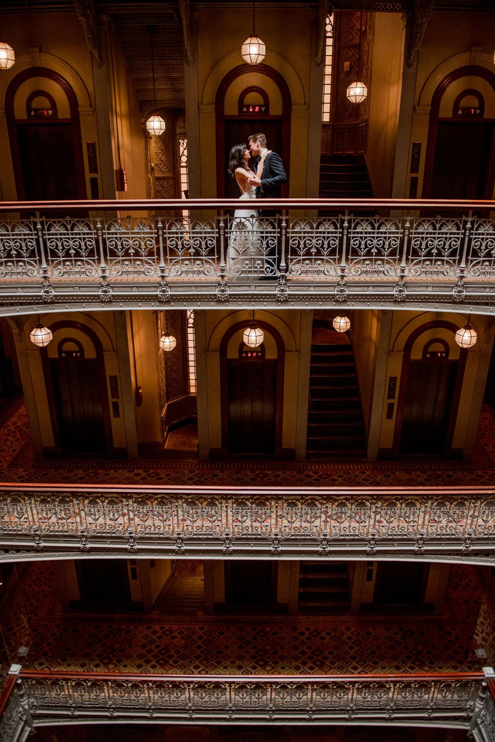 A romantic wedding moment captured on a vintage balcony with glowing pendant lights.