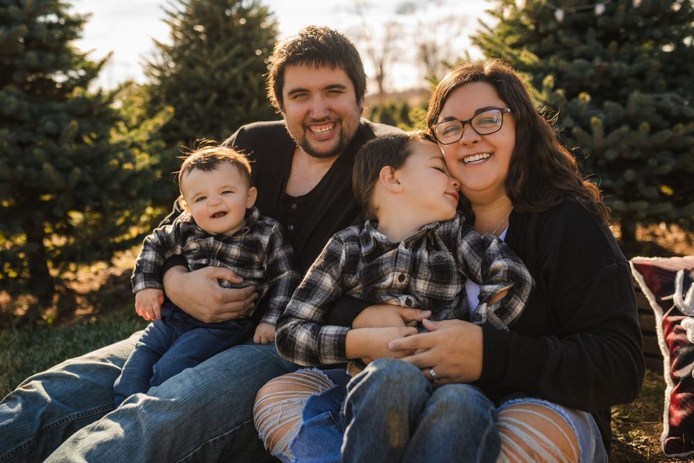 A family sits together outdoors during a photo session with evergreen trees in the background at dusk.