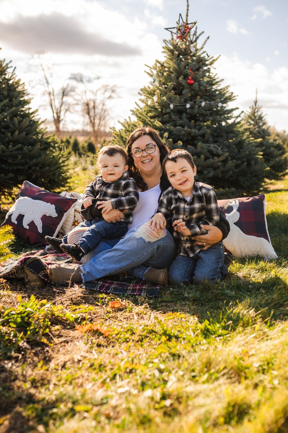 Family enjoys autumn photography session while laying in fallen leaves near evergreen trees during golden hour.