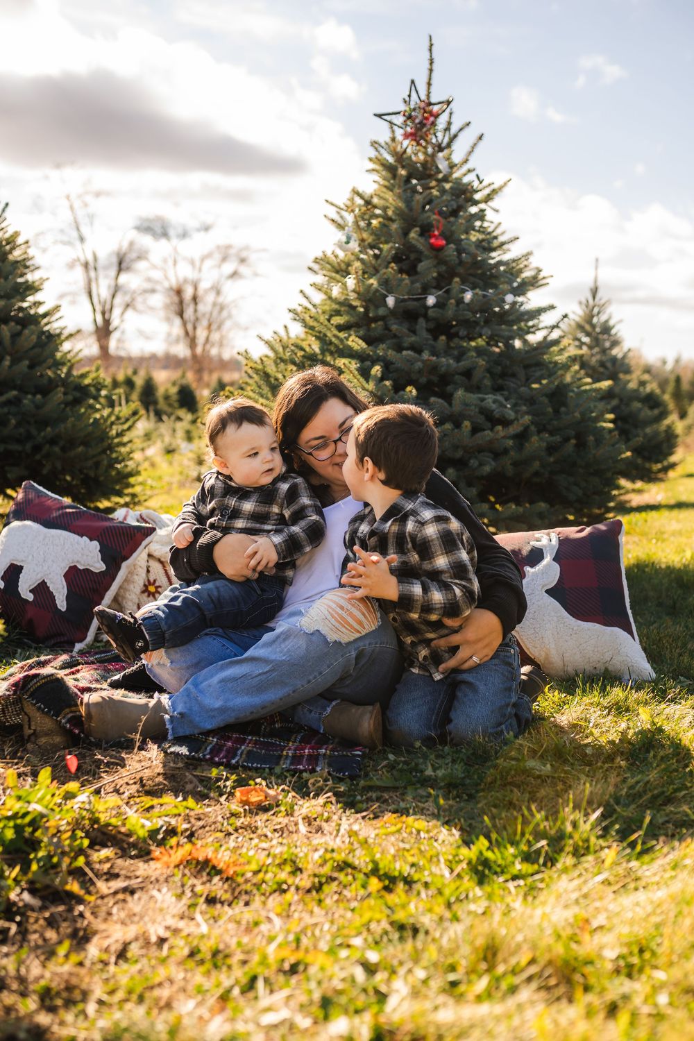 Group relaxing on blankets in autumn grass near evergreen trees during golden hour sunset.
