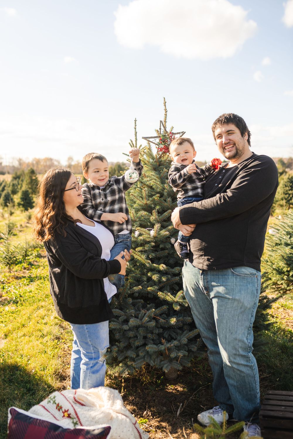 Family shares playful moments together at a Christmas tree farm during golden hour.