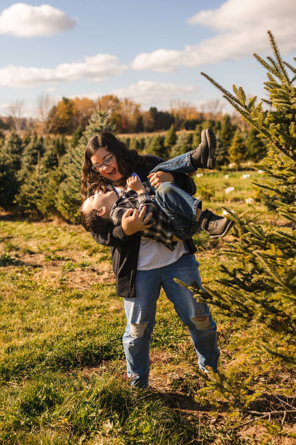 Photographers wearing backpacks capture photos of evergreen trees at a Christmas tree farm on a sunny autumn day.