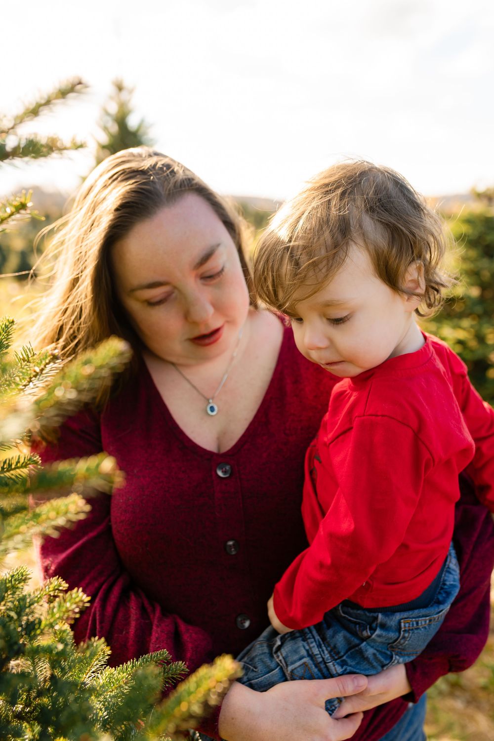 Mother and child share tender moments outdoors during golden hour in matching burgundy tops.